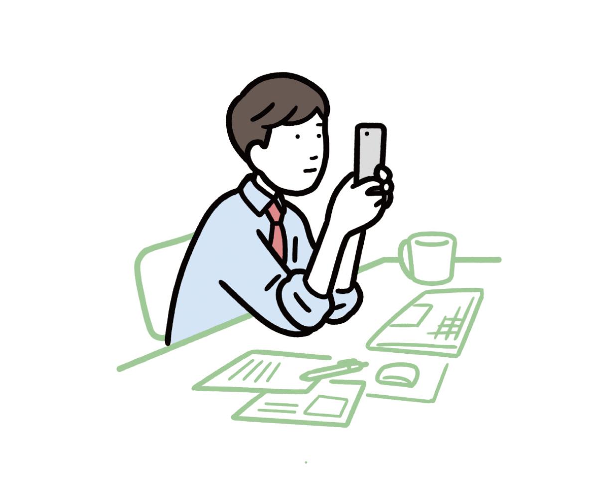 デスクに肘をついてスマホを触っている男性